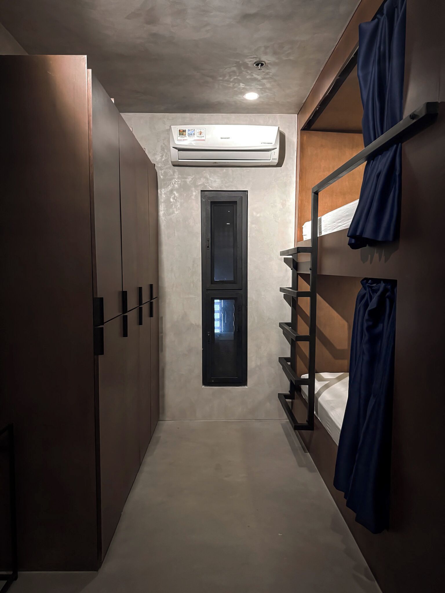 A narrow hallway with a bunk bed on the right, a wardrobe on the left, and an air conditioning unit on the ceiling.