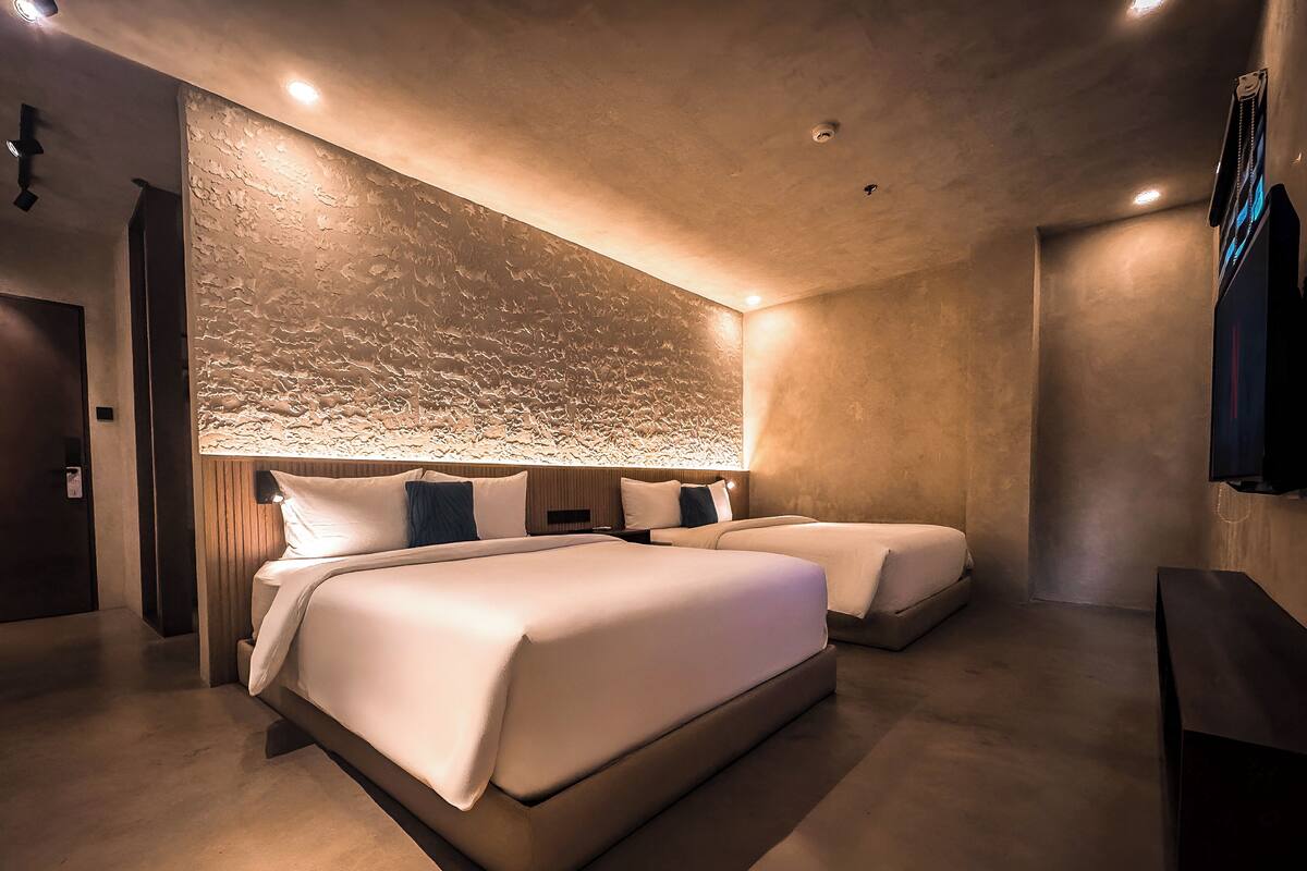 A modern hotel room with two beds, a textured wall, and recessed ceiling lights.