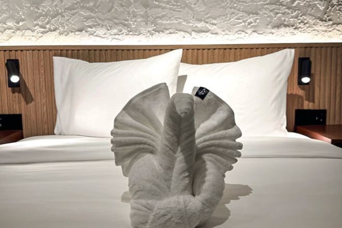 A bed with white linens and a unique white sculpture resembling a peacock.