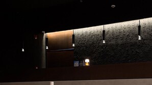A modern reception area with a wooden reception desk, two white vases with orchids, and a textured wall with integrated lighting. - Yamato Hostel (Pasay)