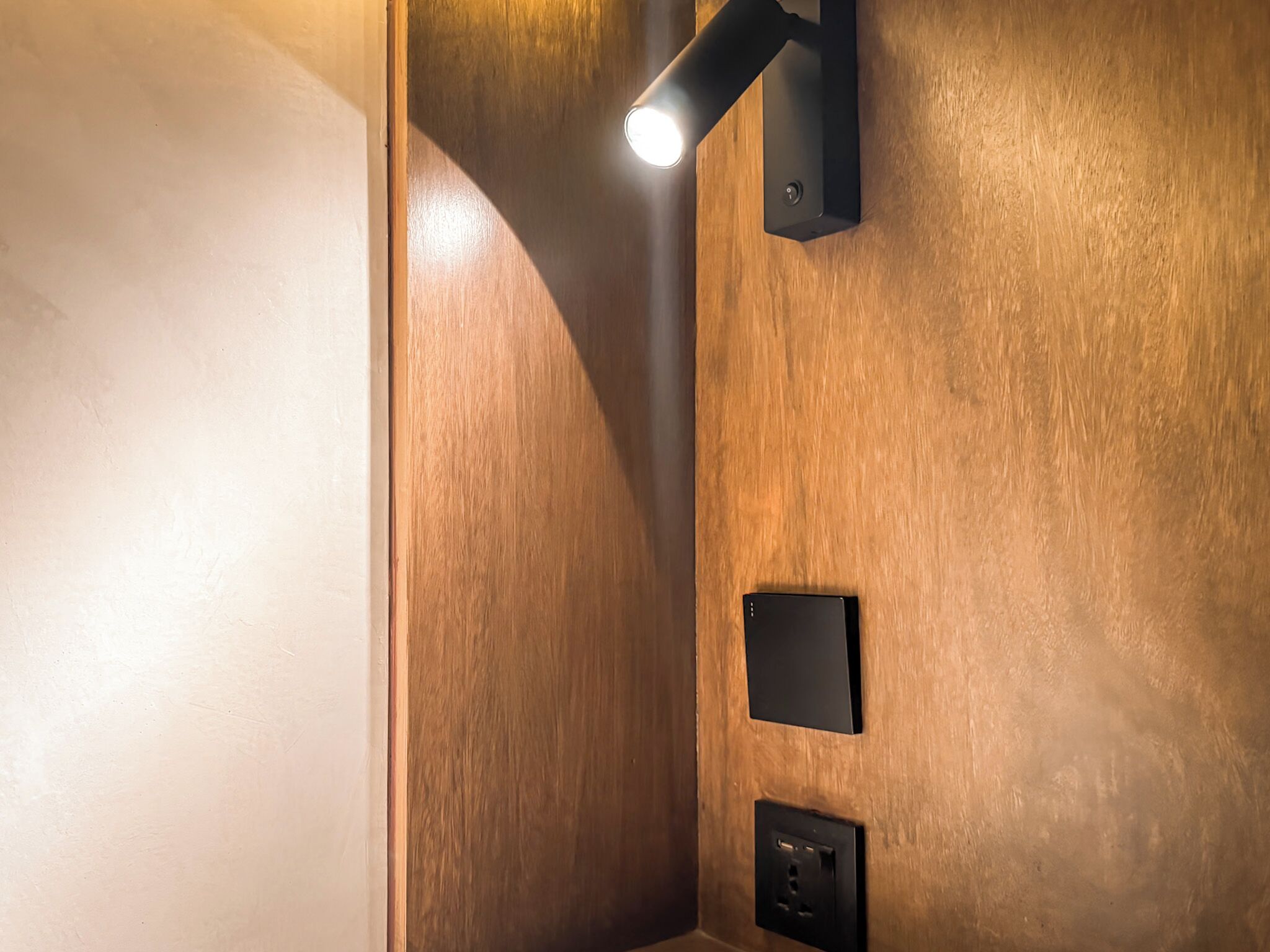 Esquina de una habitación con paredes de madera, una lámpara negra y un enchufe eléctrico negro.