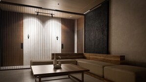 A modern, minimalist room with a wooden partition, a sofa, a coffee table, and a large dark textured wall. - Yamato Hostel (Pasay)