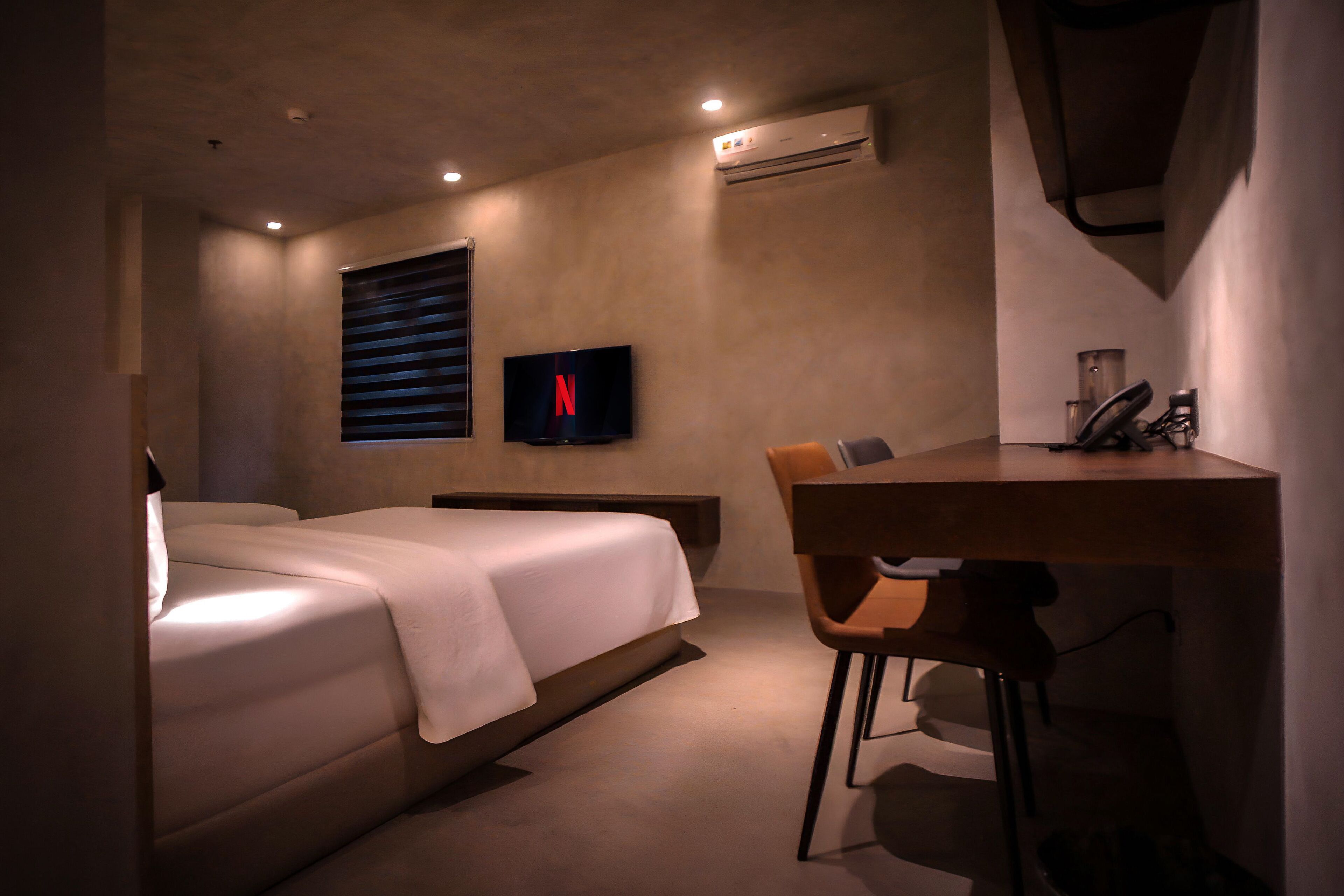 A modern bedroom with a bed, a desk, and a TV displaying the Netflix logo.