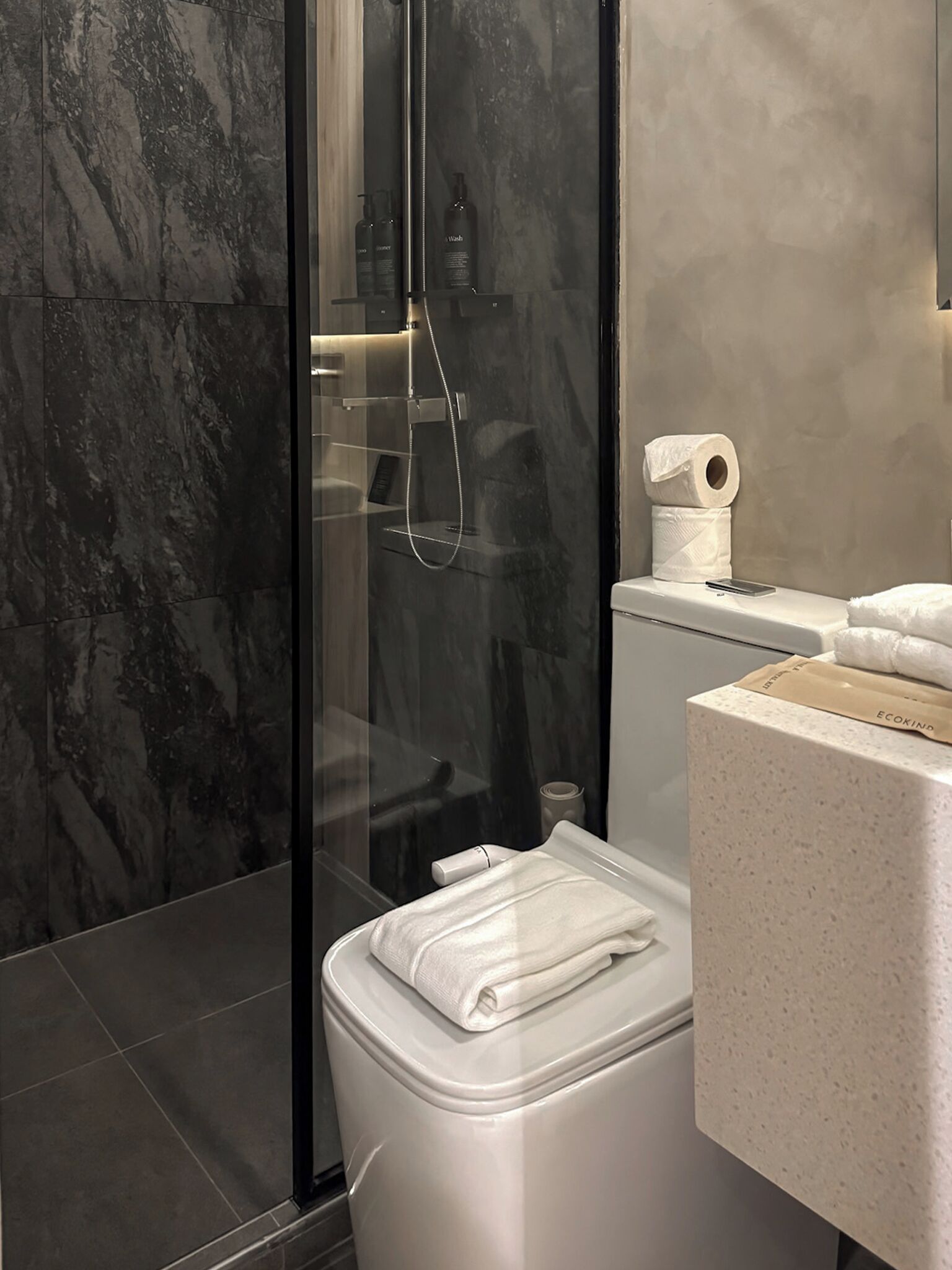A modern bathroom with a glass-enclosed shower, a toilet, and a sink area.