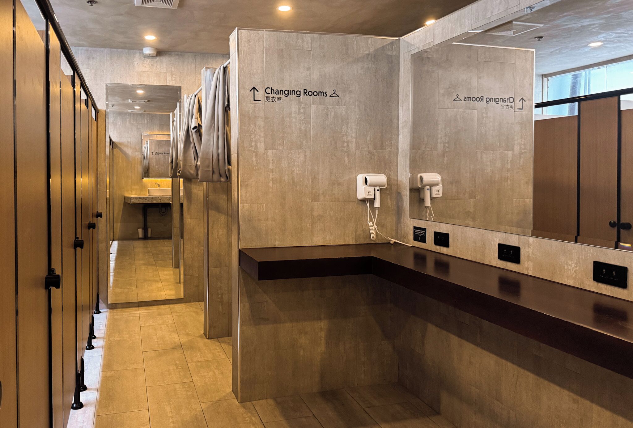 A modern changing room with mirrors, a sink, and hair dryers.