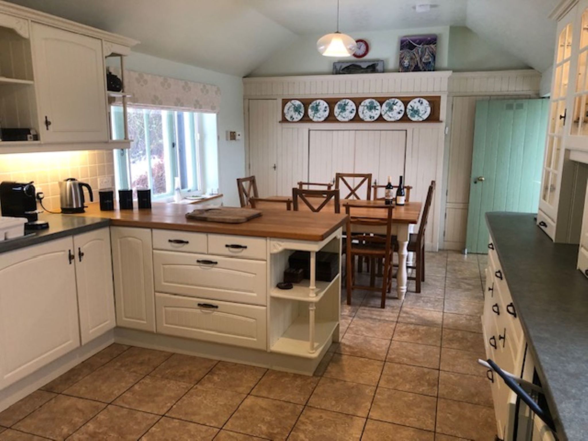 A kitchen with white cabinets, a wooden countertop, a dining table with chairs, and a hanging light fixture.