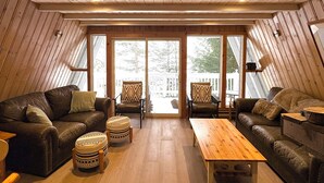 Een gezellige woonkamer met houten vloeren, een groot raam, leren banken en een houten salontafel.