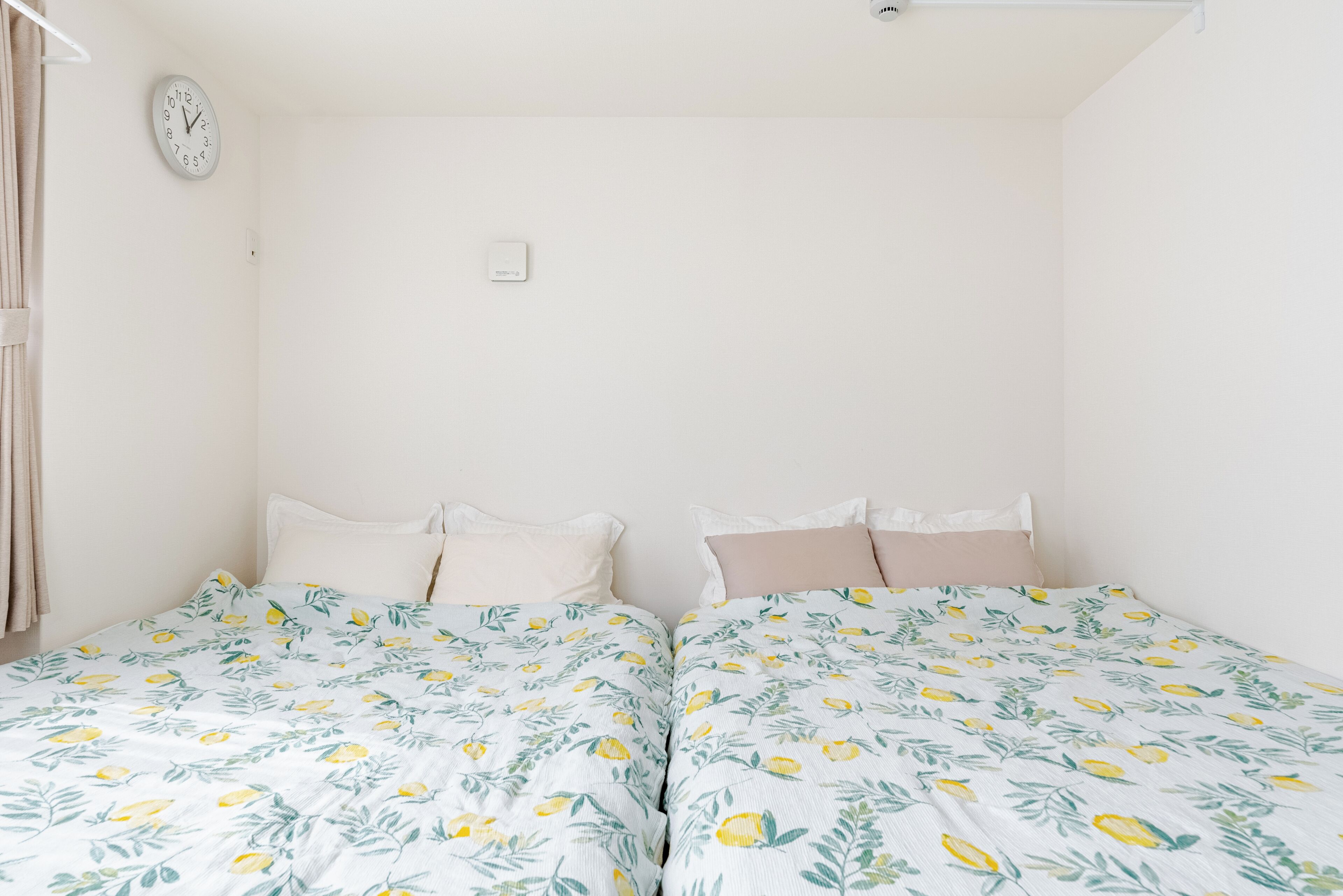 A room with two beds, each with a floral bedspread, a clock on the wall, and a thermostat.