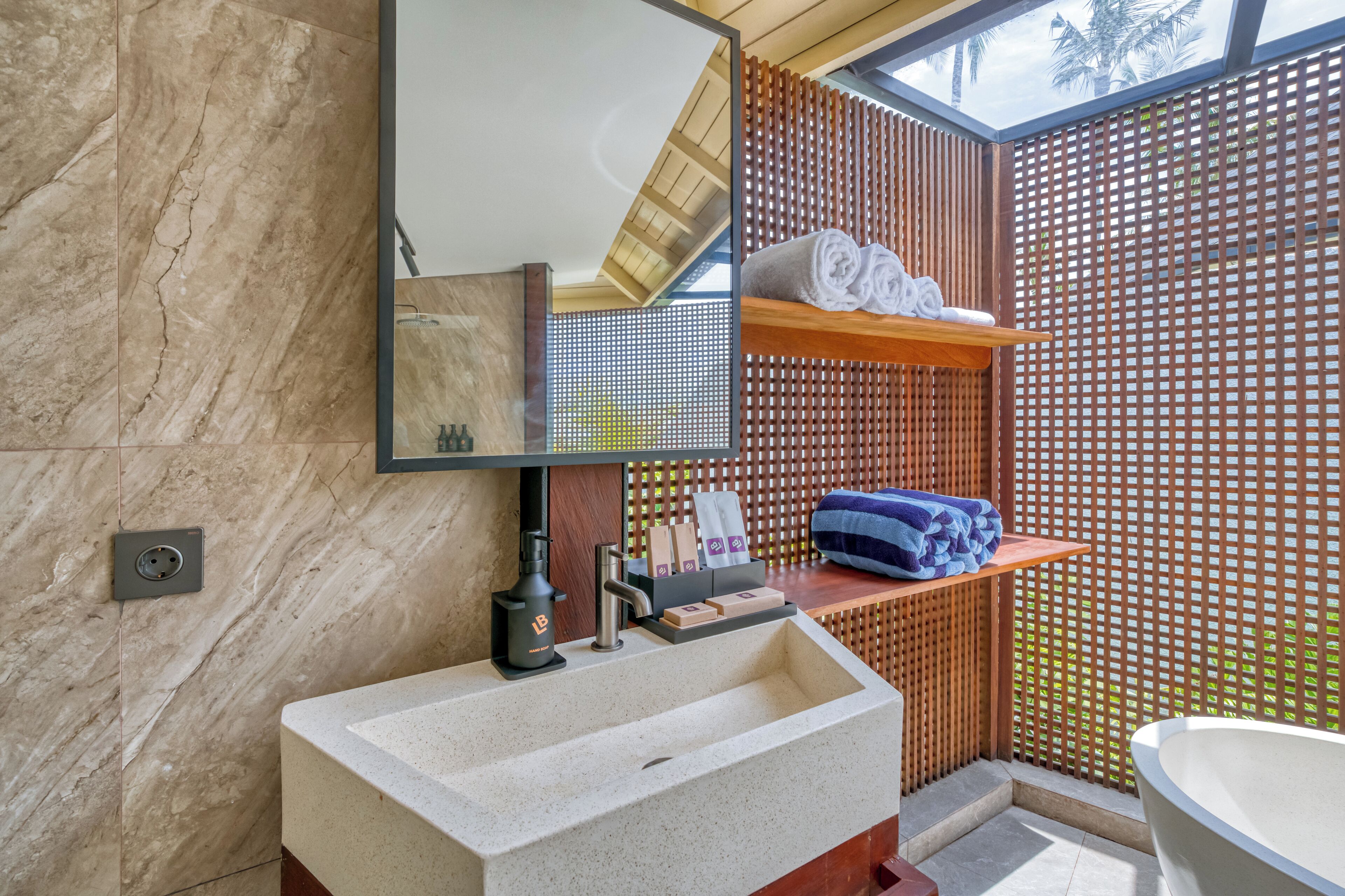 A bathroom with a marble sink, wooden shelves with towels, a wooden partition, and a large mirror.