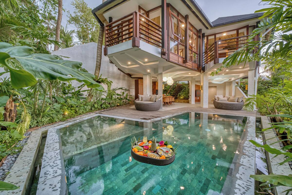 A modern house with a large glass-bottomed pool, surrounded by lush greenery.