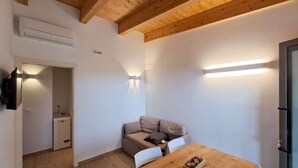 A compact room with a wooden ceiling, a white sofa, a wooden dining table with chairs, and a small kitchenette with a fridge and a washing machine. - Roseto Apartments Trilo 3 by Interhome (Roseto degli Abruzzi)