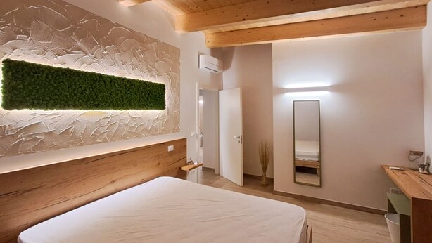 A modern bedroom with a wooden headboard, a green wall feature, a bedside mirror, and a wooden dresser. - Roseto Apartments Trilo 3 by Interhome (Roseto degli Abruzzi)