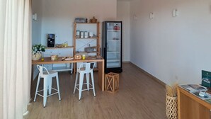 A compact kitchen with a wooden table, two white bar stools, a refrigerator, and a shelf unit with various items. - Roseto Apartments Trilo 2 by Interhome (Roseto degli Abruzzi)