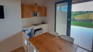 A compact kitchen with a wooden table and white chairs, a microwave, and a view of a green landscape through a glass door. - Roseto Apartments Trilo 2 by Interhome (Roseto degli Abruzzi)