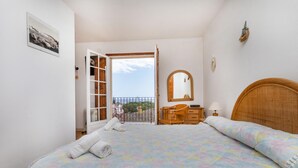 Une chambre à coucher comprenant un lit, une commode, une chaise, un miroir et un balcon avec vue.