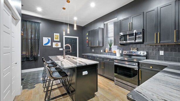 A modern kitchen with dark cabinetry, stainless steel appliances, a marble island, and bar stools. - Artsy Creative Haven Home St. Louis Art District (St. Louis)