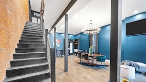 A staircase leading to a dining area with a chandelier, a TV mounted on the wall, and a brick wall on one side. - Artsy Creative Haven Home St. Louis Art District (St. Louis)
