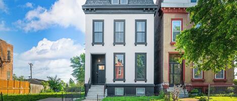 A two-story building with a black front door, a small front porch, and a brick facade.
