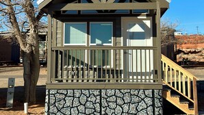 Uma cabana pequena de dois andares com base de pedra, um deck de madeira e escadas que levam à entrada.