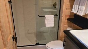 Um banheiro pequeno com box de vidro, vaso sanitário e pia com porta-toalhas acima.