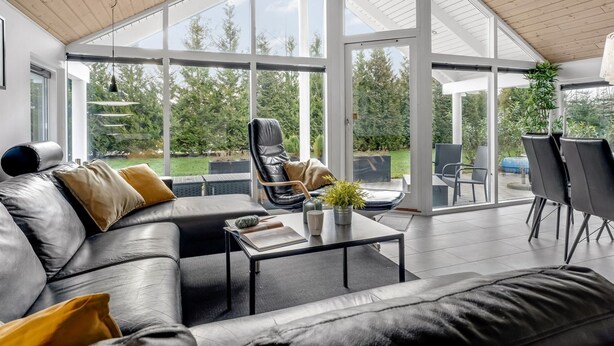 Una sala de estar moderna con un gran ventanal que da a un espacio exterior, un sofá de cuero y una mesa de centro con libros y una planta.