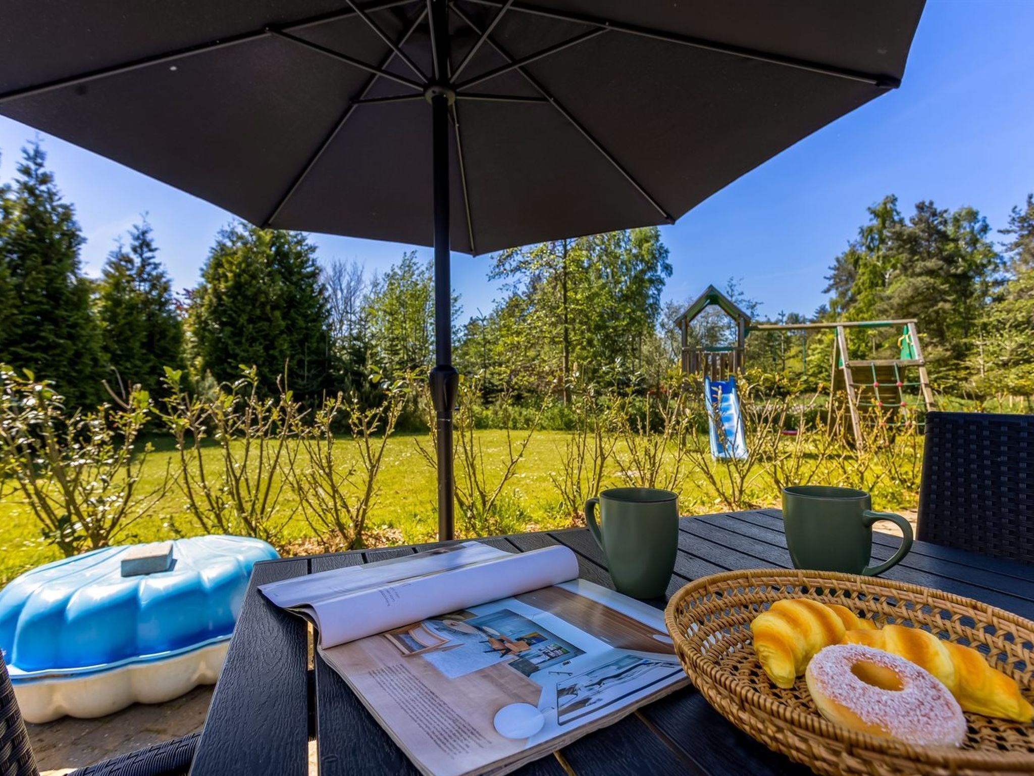 Un espace extérieur aménagé avec une table, un parasol et un panier rempli de viennoiseries.