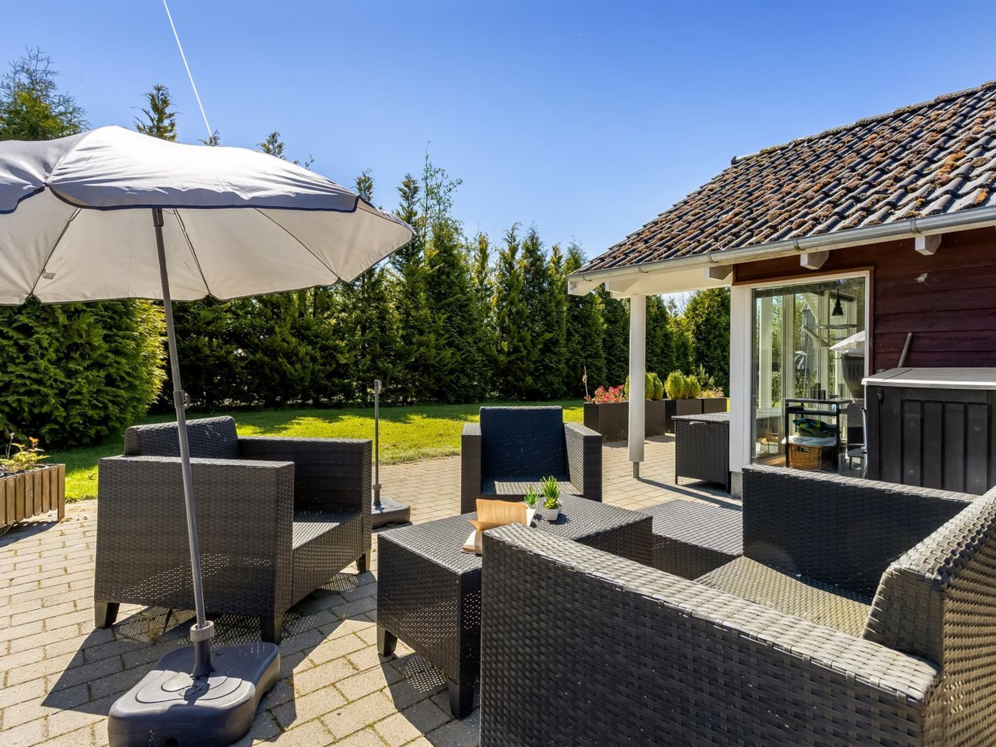 Een terras buiten met rieten meubilair, een barbecue en een overdekte zithoek.