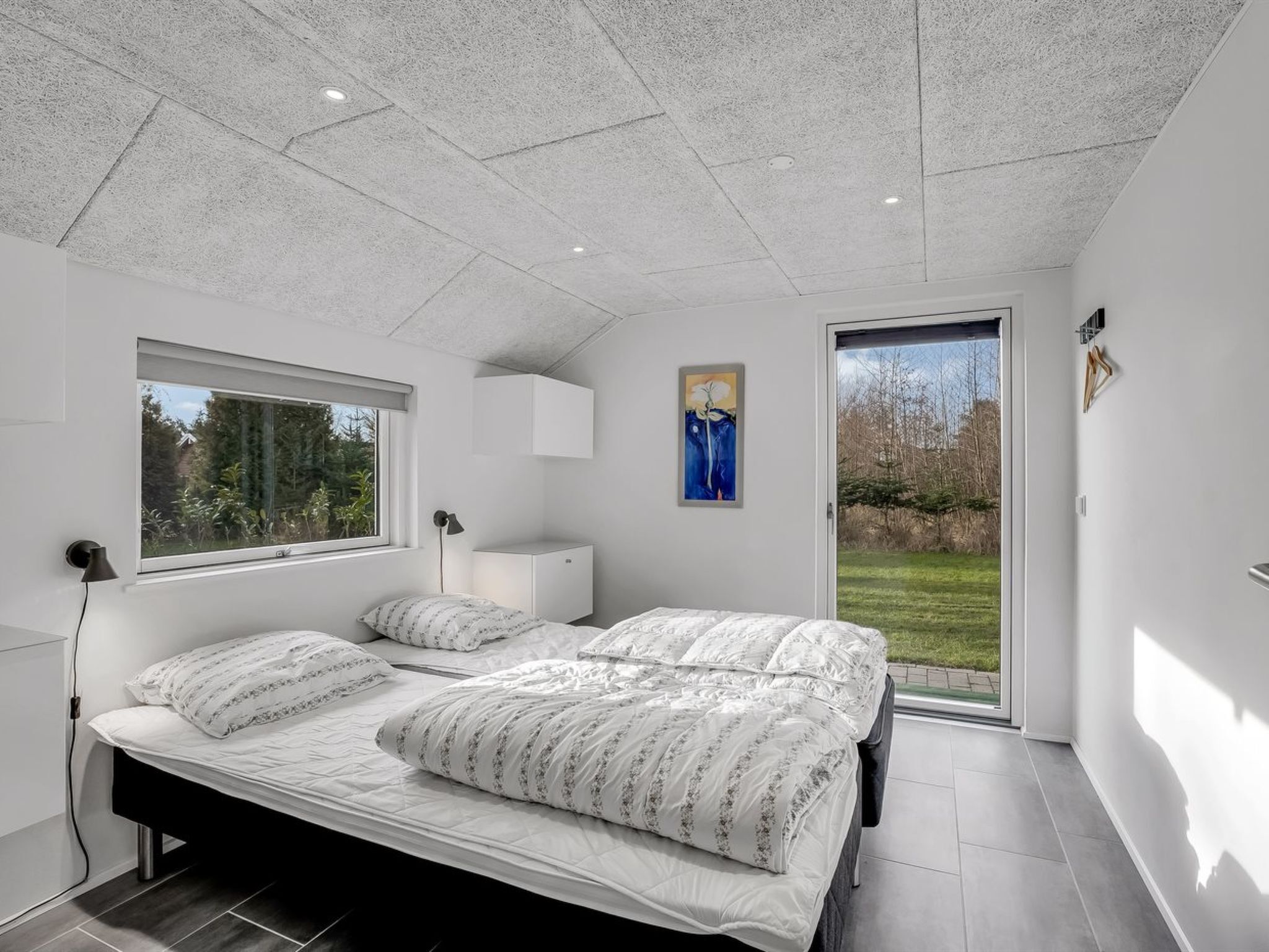 A modern bedroom with two beds, a large window, and a view of the outdoors.