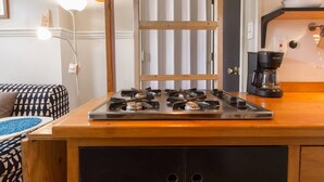 Une cuisine compacte équipée d’une cuisinière à gaz, d’une machine à café et d’un plan de travail en bois.