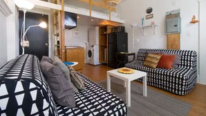 Un espace de vie compact comprenant un canapé, une petite table et un coin cuisine à l’arrière-plan.