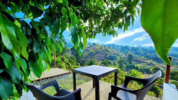 Eine Terrasse mit zwei Stühlen und einem Tisch, mit Blick auf ein üppiges Tal.