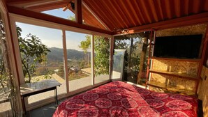 Ein Schlafzimmer mit einem großen Bett, einer Holzbalkendecke und Blick auf ein Tal durch große Fenster.