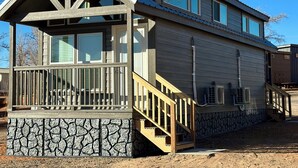A two-story house with a stone foundation, a balcony with a railing, and a staircase leading to the upper floor. - Cozy Tiny Home King Room #15B (Page)