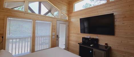 Un dormitorio con paneles de madera, una cama, un televisor montado en la pared y una ventana con persianas.