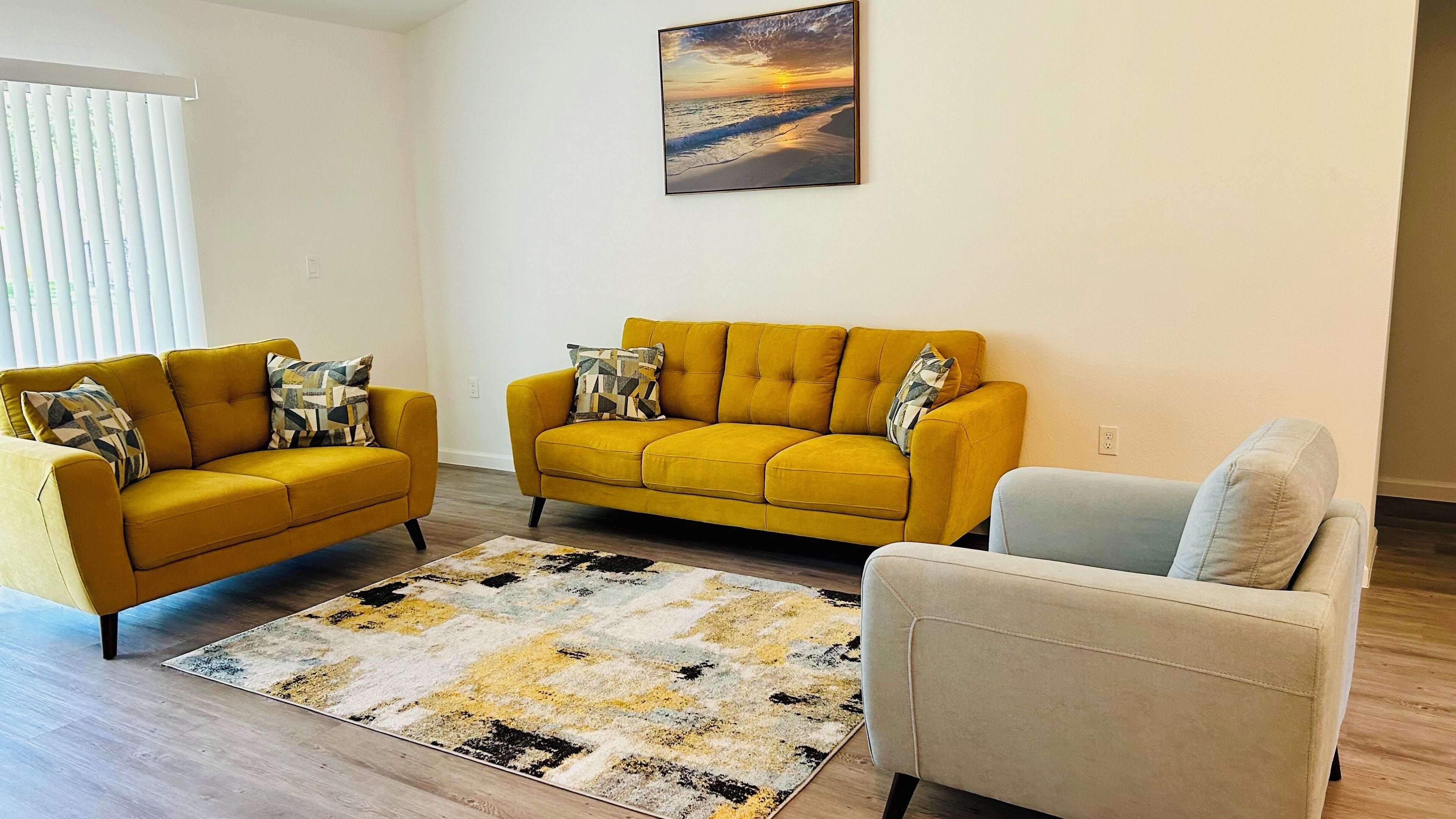 A living room with two mustard-colored sofas, a patterned rug, and a painting of a sunset.