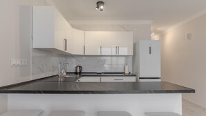 A modern kitchen with white cabinets, a black marble countertop, and a built-in island with bar stools. - Kaora Ocean View Apartment (Costa Adeje)