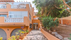 A building with a stone-paved entrance, potted plants, and a sign indicating a rental office. - Kaora Ocean View Apartment (Costa Adeje)