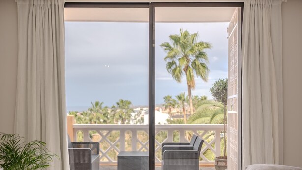 A balcony with wicker furniture, a potted plant, and a view of palm trees and the sea. - Kaora Ocean View Apartment (Costa Adeje)