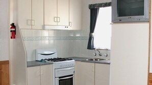 A compact kitchen with white cabinets, a gas stove, a built-in oven, a sink, and a television mounted above it. - Elliston Waterloo Bay Tourist Park  (Elliston)