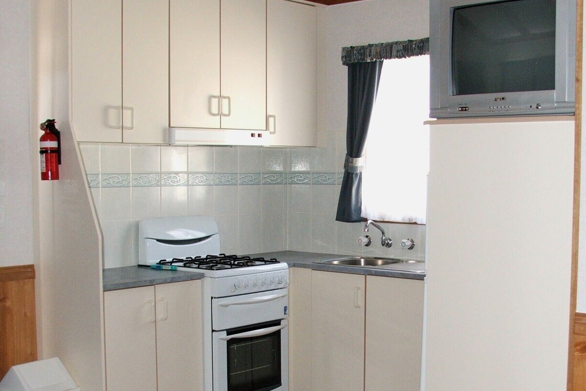 A compact kitchen with white cabinets, a gas stove, a built-in oven, a sink, and a television mounted above it.