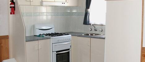 A compact kitchen with white cabinets, a gas stove, a built-in oven, a sink, and a television mounted above it.