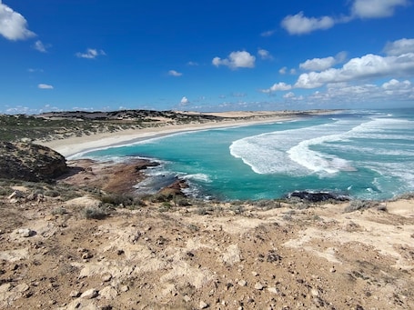A coastal landscape with a sandy beach, rocky terrain, and clear blue waters.. Elliston Waterloo Bay Tourist Park