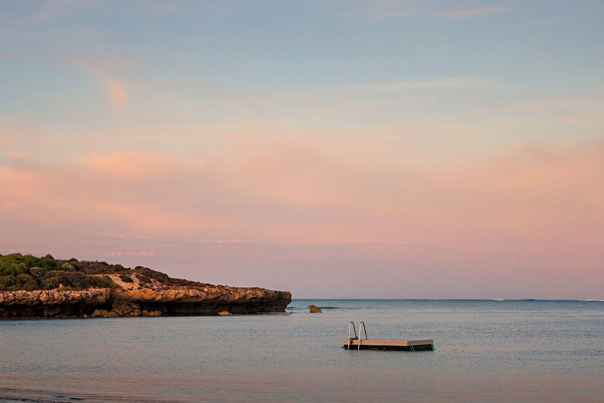 Un mar tranquilo con un litoral rocoso y un pequeño muelle.
