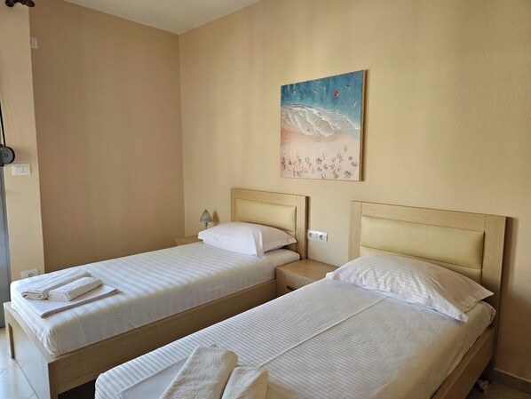 Habitación de hotel con dos camas individuales, una mesita de noche con lámpara y un cuadro en la pared.