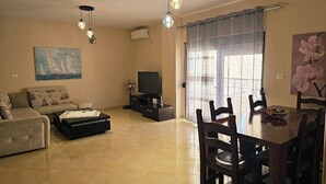 Una sala de estar con sofá, televisor, mesa de comedor, sillas y un cuadro en la pared.