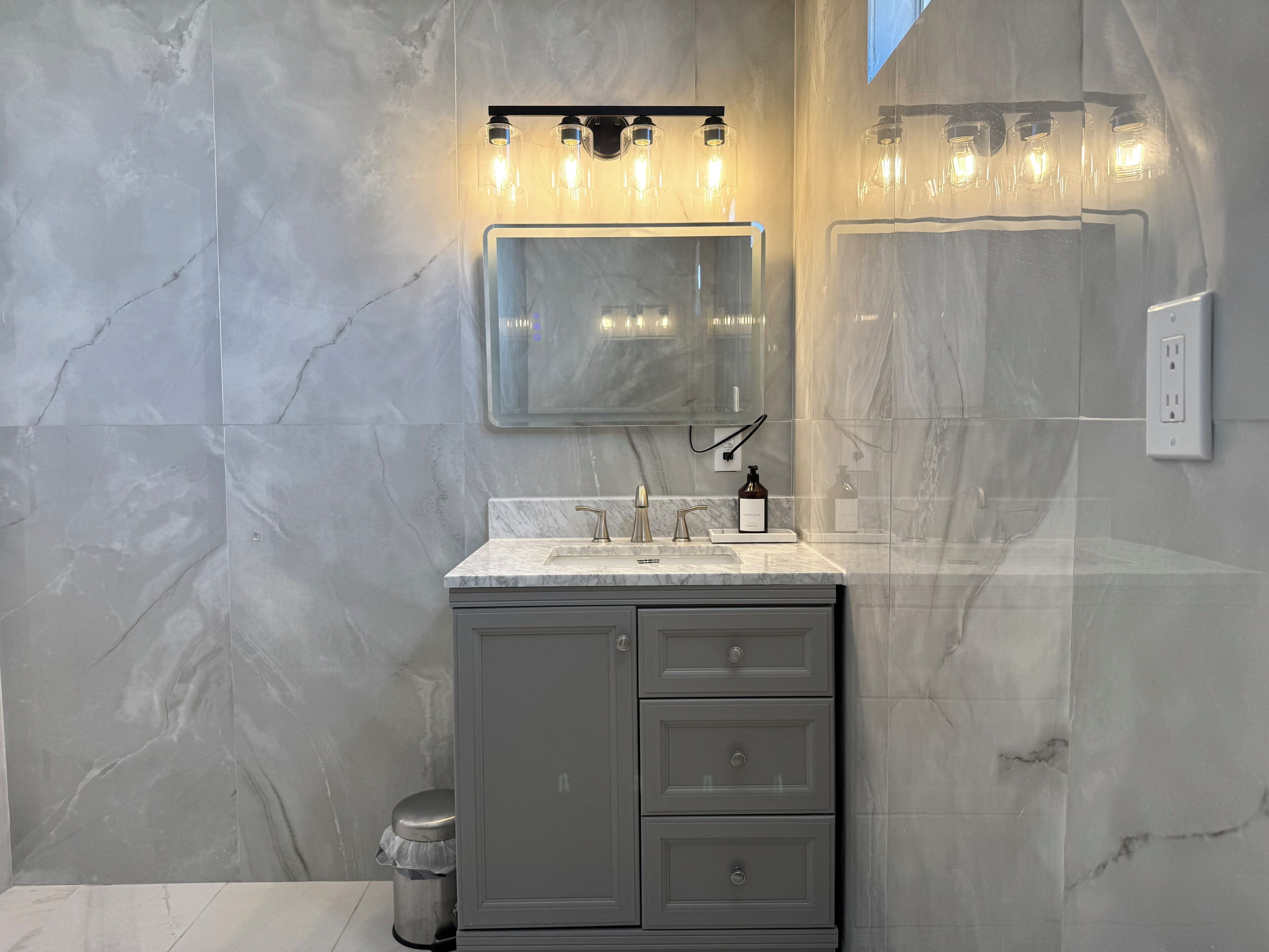 Un baño moderno con tocador de mármol, un espejo y una lámpara sobre el espejo.