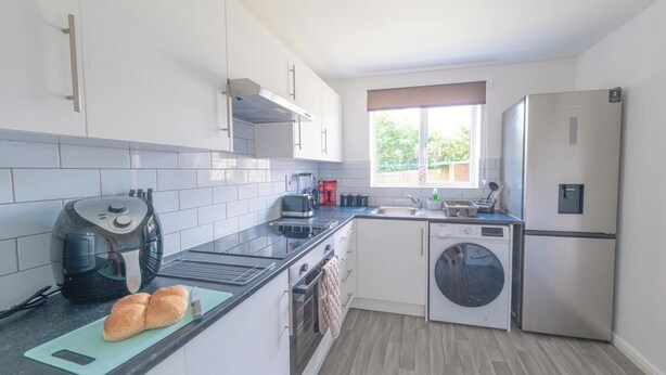 A compact kitchen with a built-in oven, a washing machine, and a refrigerator. - Sleeps 5 - Private Garden- Free Parking (Corby)