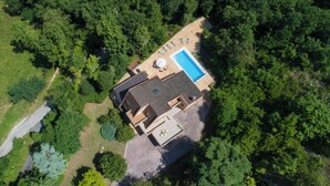 Vista aérea de uma casa com piscina, rodeada por uma floresta densa.