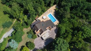 An aerial view of a house with a swimming pool, surrounded by dense forest.