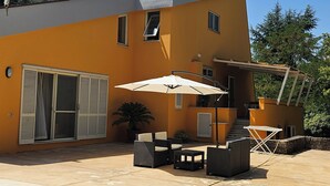 Uma casa moderna com um alpendre, móveis de exterior e um grande guarda-sol.